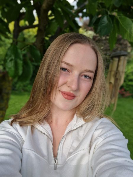 Rosa Eine Frau mit blonden Haaren, die ein Selfie vor einem grünen Baum in einem grünen Garten macht